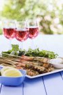 Grilled prawn skewers with garlic butter and glasses with red wine on background outdoors — Stock Photo