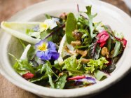Смешанный салат с съедобными цветами и грибами шантерель на белой тарелке — стоковое фото