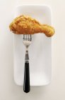 Closeup top view of fried drumstick on fork and white dish — Stock Photo