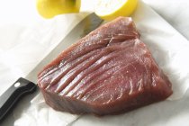 Raw tuna with knife and lemons — Stock Photo