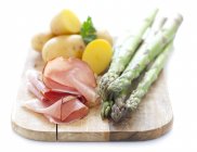 Green asparagus, ham and potatoes on a chopping board — Stock Photo
