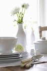Vaisselle empilée et couverts sur une table avec un vase de fleurs blanches de ranunculus — Photo de stock