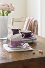 Piatti impilati e tazze di caffè vicino rosa fiori Ranunculus in un vaso — Foto stock