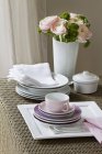 Vue surélevée des assiettes empilées et des tasses à café avec un bouquet de fleurs de ranunculus roses — Photo de stock