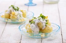 Closeup view of potato salad with hard-boiled eggs, sour cream, fennel and chives on glass plates over wooden surface — Stock Photo