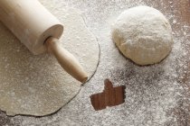 Closeup view of rolled-out pastry with a rolling pin, a ball of dough and flour with a like symbol — Stock Photo