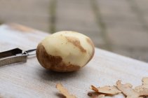 Pommes de terre partiellement pelées avec éplucheur — Photo de stock