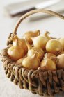 Lots of small onions in a basket over white surface — Stock Photo