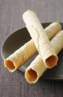 Closeup view of three rolled wafers on black plate — Stock Photo