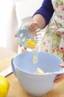 Closeup view of woman adding egg to dough mixture in bowl — Stock Photo
