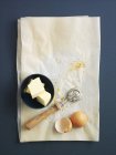 Vista superior de la mantequilla con una rueda de pastelería y cáscaras de huevo en papel a prueba de grasa - foto de stock