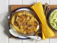 Janssons frestelse - рагу с картофелем, луком и анчоусами на тарелке над деревянным столом — стоковое фото