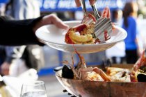 Cropped view of person serving lobster from wooden bowl with tongs — Stock Photo