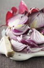 Cipolle rosse, tagliate a metà e a spicchi su tagliere con coltello — Foto stock