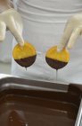 Close-up vista cortada de chocolatier mergulhando fatias de laranja cristalizadas para chocolate derretido — Fotografia de Stock