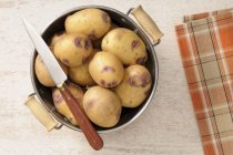 Свежий картофель в дуршлаге с ножом — стоковое фото