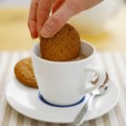 Mão feminina derramando biscoito no chá — Fotografia de Stock