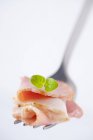Sliced ham with oregano leaf on fork — Stock Photo