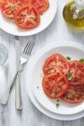 Tomato salad with olive oil on white plates over wooden surface with fork and knife — Stock Photo