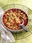 Closeup view of strawberry crumble in baking dish with towel and spoon — Stock Photo