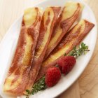Closeup view of four pieces of vegetarian bacon with raspberries — Stock Photo