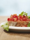 Bruschetta con pomodori e rucola su piastra bianca su superficie in legno — Foto stock