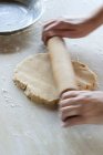 Vue rapprochée des mains rouler la pâte courte croûte avec un rouleau à pâtisserie — Photo de stock