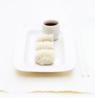 Крупный план белой тарелки с тремя пельменями и белым рамекином соевого соуса — стоковое фото
