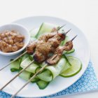 Skewers of chicken, served with cucumber slices and a satay side-dish on white plate — Stock Photo