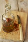 Olio d'oliva infuso con peperoncini secchi su scrivania in legno con bottiglia e coltello — Foto stock