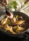 Cropped view of hand pouring red wine on chicken in frying pan — Stock Photo