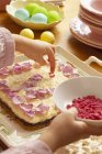 Geschnittene Ansicht der Person, die Masurek-Torte mit Blütenblättern und getrockneten Erdbeerstücken dekoriert — Stockfoto