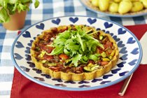 Vegetable tart with rocket in white and blue plate over red towel — Stock Photo