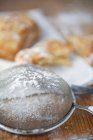 Primo piano vista di setaccio con zucchero a velo e pasticcini al forno sullo sfondo — Foto stock