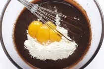 Nahaufnahme von Ei mit Schneebesen und Mehl in geschmolzener Schokolade — Stockfoto