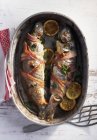 Trout wrapped in bacon in roasting tin — Stock Photo