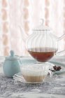 Чай латте в скляній чашці перед скляним чайником — стокове фото
