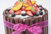 Vista de cerca de la torta de chocolate con fruta fresca, azúcar glaseado y una cinta rosa - foto de stock