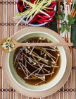 Broth with enoki mushrooms and vegetables on plate with wooden spoon — Stock Photo
