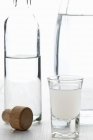 Closeup view of Ouzo after water dilution with Ouzo bottle and carafe of water — Stock Photo