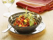 Ratatouille with rosemary and basil in bowl over plate — Stock Photo