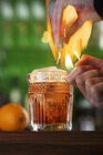 Closeup cropped view of hands flaming cocktail with orange — Stock Photo