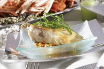 Roast turbot with vegetables in glass bowl over plate — Stock Photo