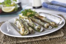 Жареные моллюски с чесноком и петрушкой на белой тарелке на соломенном коврике — стоковое фото