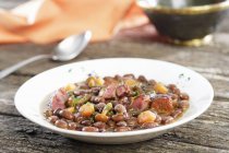 Stew, light speckled kidney beans, chorizo, mushrooms, bacon in white plate over wooden surface — Stock Photo