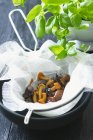 Closeup view of assorted mushrooms in a muslin cloth in a sieve and fresh basil — Stock Photo