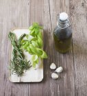 Базилік, розмарин і часник - інгредієнти для нанесення оливкової олії на дерев'яну поверхню з пляшкою — стокове фото