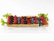 Closeup view of rectangular mixed berry tart on a glass tray garnished with mint leaves — Stock Photo