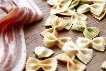 Uncooked bacon and colored farfalle pasta — Stock Photo