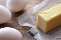 Vista de cerca de la barra de mantequilla en papel y huevos - foto de stock